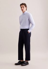 Lichtblauw-wit gestreept overhemd met knopen en een kraag, gecombineerd met marineblauwe broek. Zwart veterchoenen maken de outfit compleet.