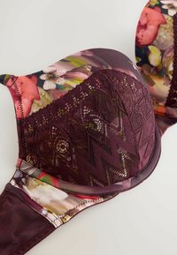 Blomster bh med polstrede skåle, der har en burgunder lace overlay og multikolore blomsterprint på stropperne og båndet mod en hvid baggrund.