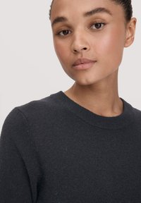 Dunkelgrauer Strickpullover mit rundem Ausschnitt, der eine glatte Textur und eine taillierte Passform aufweist, teilweise von einer Person getragen.