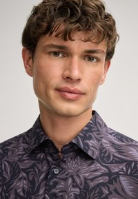 Langärmeliges Hemd mit dunkler Grundfarbe und detailiertem lila Blumenmuster. Hat einen strukturierten Kragen und eine Knopfleiste, gefertigt aus gewebtem Stoff.