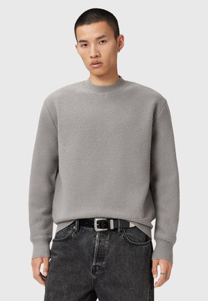 Grå crewneck sweater med tekstureret overflade, ribstrikkede manchetter og kant, båret over mørke jeans med et sort bælte. Enkel og moderne design.