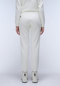 Witte joggingsbroek met een relaxte pasvorm, elastsiche enkels en een bijpassend topje, gecombineerd met lichte schoenen. Zachte, gladde stoftextuur.