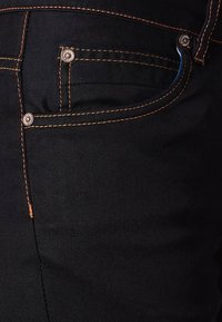 Czarne jeansy z denimu z miedzianym szwem, detalami na guziki i dopasowanym krojem. Tekstura wydaje się gładka, z minimalnymi oznakami zużycia.