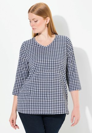 Yhtenäinen sinivalkoinen houndstooth-kuvioinen paita, jossa on V-kaulus, kolmasosa hihat ja rento istuvuus. Pehmeä kangas, jossa on hienovarainen tekstuuri.