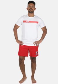 Hvid t-shirt med røde vandrette striber og teksten "VIVID". Røde badebukser med et sort palmetræ-logo. Casual pasform, letvægtsstof.