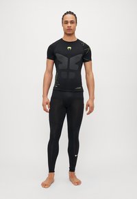 Camisa de compresión atlética negra de manga corta con paneles texturizados, combinada con leggins negros ajustados que presentan un logotipo blanco.