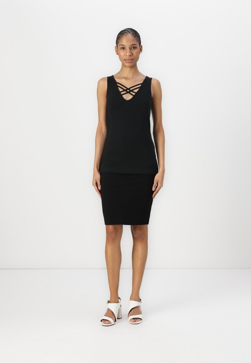 Musthave musta tank top, millel on ristkülikuteta disain kaeluse juures, kombineerituna musta pliiatsseeliku ja valgete plokknööridega sandaalidega.