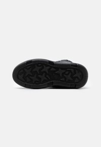 Svart sneaker sula med texturerad gummi, med ett stjärnmönster för grepp. Rund form med slät kant och djupa spår.