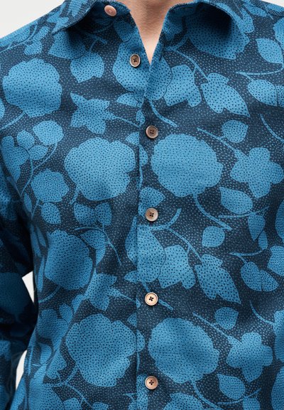 Μπλε πουκάμισο με σκούρο μπλε λουλουδένιο μοτίβο και ανοιχτό καφέ κουμπιά, φορεμένο από άτομο που φαίνεται από τον λαιμό μέχρι τη μέση.