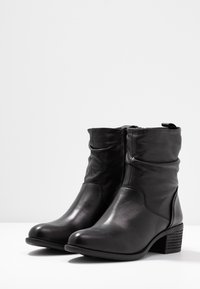 Bottes de cheville en cuir noir avec un design plissé, un talon bas et empilé, et une texture lisse. Comprend une fermeture éclair latérale et de simples détails de coutures.