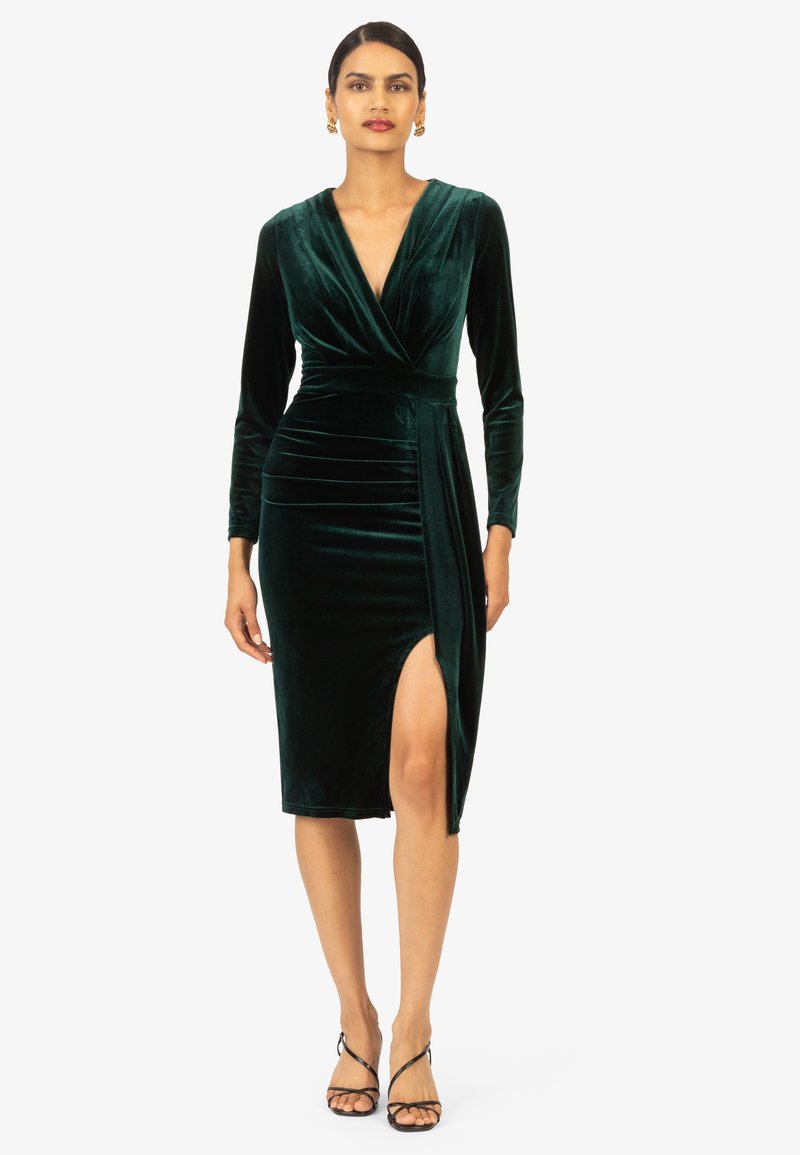 Smaragdgroene fluwelen jurk met lange mouwen, V-hals en een zijslit, met een getailleerd silhouet en gathered details bij de taille.