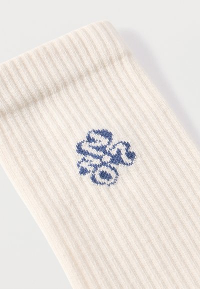 Ύφασμα σε εκρού ριμπ με μικρό, μπλε κεντητό αφηρημένο λουλουδένιο σχέδιο κοντά στην διπλωμένη άκρη.