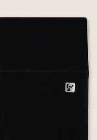 Leggings neri realizzati in tessuto elasticizzato con una superficie liscia, dotati di una piccola etichetta logo in argento e di una cintura cucita.