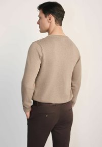 Beżowy sweter z dzianiny, z długimi rękawami, okrągłym dekoltem i gładką fakturą, zestawiony z ciemnobrązowymi spodniami z detalami kieszeni i paskiem.