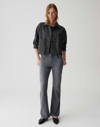 Geknipte, donkergrijze gestructureerde jas met grote zakken, knoopsluiting, gecombineerd met grijze flared jeans en zwarte puntige schoenen.