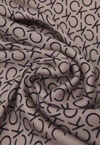 Tessuto Calvin Klein, beige con motivo ripetuto delllogo "CK" in nero, texture liscia, leggero e che si drappeggia dolcemente.