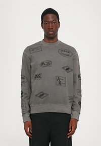 Šedá mikina vyrobená z bavlny, s různými černými nášivkami s logem "Armani Exchange". Hladký límec a manžety, uvolněný střih.
