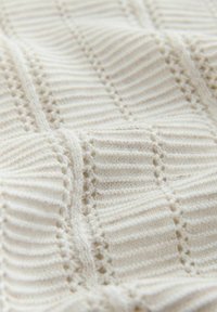 Cremefarbener Strickstoff mit gerippten und durchbrochenen vertikalen Streifen, die ein strukturiertes Muster bilden.