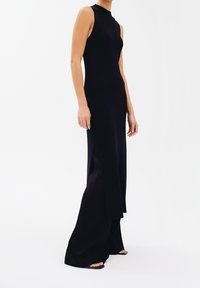 Abito nero a costine con collo alto, design senza maniche e spacchi laterali, creando una silhouette fluida. Aspetto semplice e moderno.