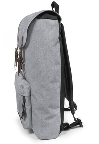 Zaino in tessuto grigio con parte superiore arrotondata, dettagli neri, spallacci regolabili e maniglie in pelle marrone sul cappuccio. Tasca laterale in rete visibile.