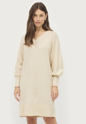 Beige gebreid jurkje met een V-hals, ballonmouwen en geribbelde manchetten en zoom. Gladde textuur, knielange ontwerp, subtiele kleurvariaties.