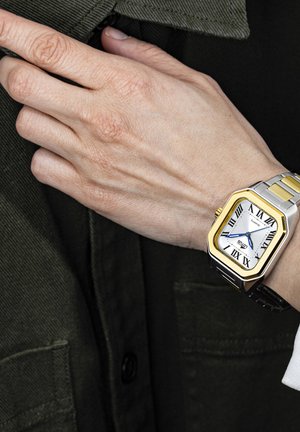 Orologio argento e oro con quadrante bianco e numeri romani, caratterizzato da una cassa rettangolare, lancette blu e un cinturino nero.
