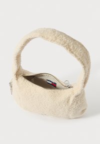 Béžová kabelka vyrobená ze strukturovaného fleecu s krátkým, zakřiveným úchopem a zapínáním na zip. Uvnitř je značená štítek.