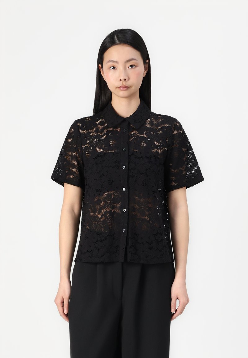 Chemise noire en dentelle à manches courtes avec un col, ornée de motifs floraux, fermeture à boutons à l'avant et texture semi-transparente.
