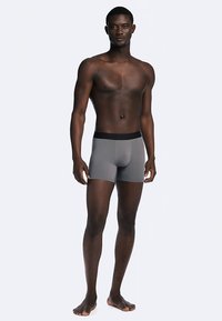 Boxer grigi in tessuto liscio, con una fascia elastica nera in vita. Il modello è aderente e arriva a metà coscia.