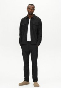 Black textured jacket with two front pockets, paired with matching black trousers and beige slip-on shoes. White T-shirt underneath.