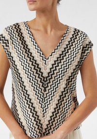Korte mouwen V-hals top met een zigzagpatroon in zwart, wit en beige. Gemaakt van een gestructureerde stof met een ontspannen pasvorm.