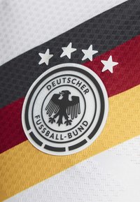 Wit en zwart gestructureerde stof toont het logo van de Duitse Voetbalbond, met een zwarte arend en vijf sterren boven rode en gele strepen.