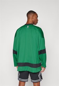 Zöld kosárlabda mez fekete akcentusokkal és kerek nyakkal. Az anyaga légáteresztő hálószövetnek tűnik, laza fazonnal. NBA logó a gallérnál.