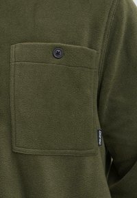 Groene fleece shirt met een borstzak en zwarte knoop. Zachte textuur en een label met "BLEND" op de zijnaad.