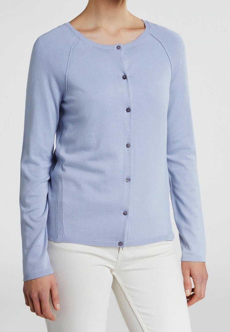 Cardigan bleu clair en tissu doux, avec des manches longues, un col rond, et une fermeture à boutons à l'avant avec des boutons foncés.