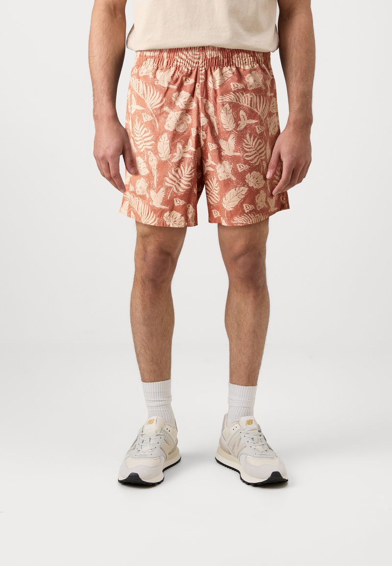 Cotton swim shorts in coral with an all-over cream tropical leaf pattern, elastic waistband, and straight-cut hem. Worn with white sneakers.