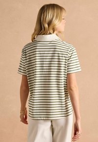 Kreemikaaluses lühikeste varrukatega polo särk, millel on rohelised horisontaalsed triibud, klassikaline krae ja külgedel lõhikute disain, mis tagab liikumisvabaduse.