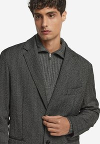 Grau gestreifter Blazer mit zwei Knöpfen, Reverskragen und einer Brusttasche. Darunter getragen mit einem grauen gerippten Pullover.