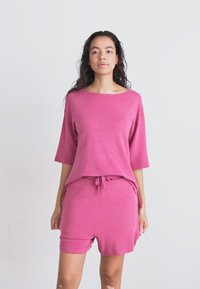 Ροζ σετ χαλάρωσης που αποτελείται από ένα χαλαρό, κοντομάνικο μπλουζάκι και ταιριαστά σορτσάκια με ρυθμιζόμενη μέση, φτιαγμένο από μαλακό, υφασματισμένο ύφασμα.