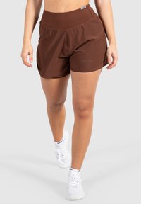 Bruna träningsshorts med bred midjeband, lättviktsmaterial och sidofickor. Tillsammans med vita sneakers som har nätdesign.
