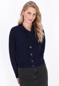 Navy blue knitted cardigan with a tied neck detail, button front closure, and long sleeves; soft texture with a slightly fitted shape.