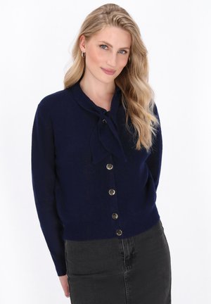 Navy blue knitted cardigan with a tied neck detail, button front closure, and long sleeves; soft texture with a slightly fitted shape.