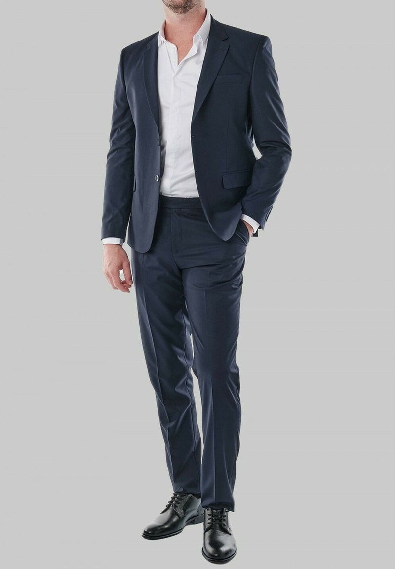 Costume marine avec un design ajusté, veste à un bouton, revers en angle, associé à une chemise blanche et des chaussures en cuir noires. Texture de tissu lisse.