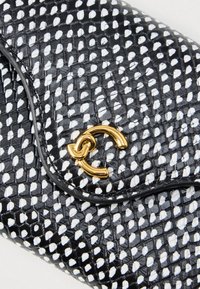 Juodas ir baltas tekstūruotas odinis piniginė su auksiniu tarpusavyje susijungiančiu CC logotipu ant užsegimo.