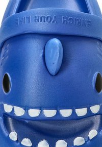 Zuecos de goma azules con un diseño de cara de tiburón sonriente, con dientes blancos y un acabado texturizado. Tiene dos agujeros de ventilación.