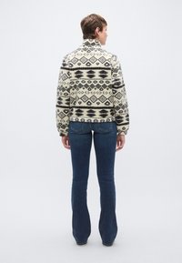 Jakna od mješavine vune s geometrijskim crno-krem uzorkom, visokim ovratnikom i opu�štenim krojem. Uparena s tamnoplavim trapericama širokih nogavica.