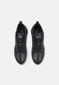 Svarta sportskor med meshdesign, texturerad ovandel, reflekterande accenter och en vit sula. Sex snörningsöglor säkrar foten.