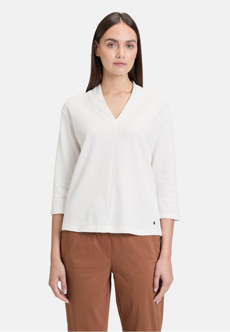Top bianco a maglia rigata con scollatura a V e maniche a tre quarti, caratterizzato da una vestibilità rilassata e un piccolo logo sul fondo.