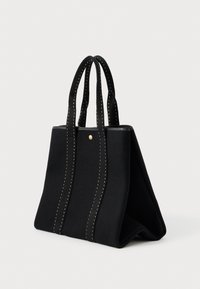 Μαύρη τσάντα tote φτιαγμένη από μαλακό υλικό, με αντίθετη λευκή ραφή, δομημένο σχήμα, δύο λαβές και μια μικρή χρυσή λεπτομέρεια.