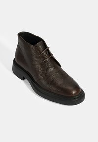 Donkerbruin, gestructureerd leren enkelboot met zwarte zool en vetersluiting, in een schuine kijk op een witte achtergrond.